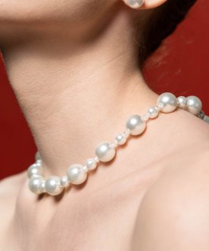 Close-up of a woman's neck adorned with a pearl necklace against a red background.