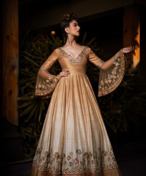 Woman in elegant golden gown with embroidered sleeves.